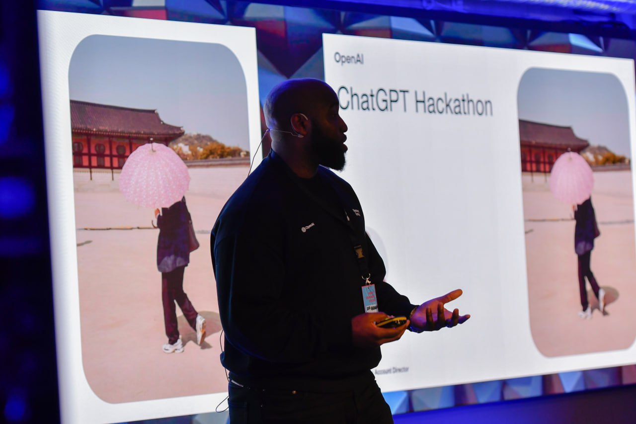 A presenter on stage in front of a slide reading 'OpenAI — ChatGPT Hackathon' at Product Management Days 2025.