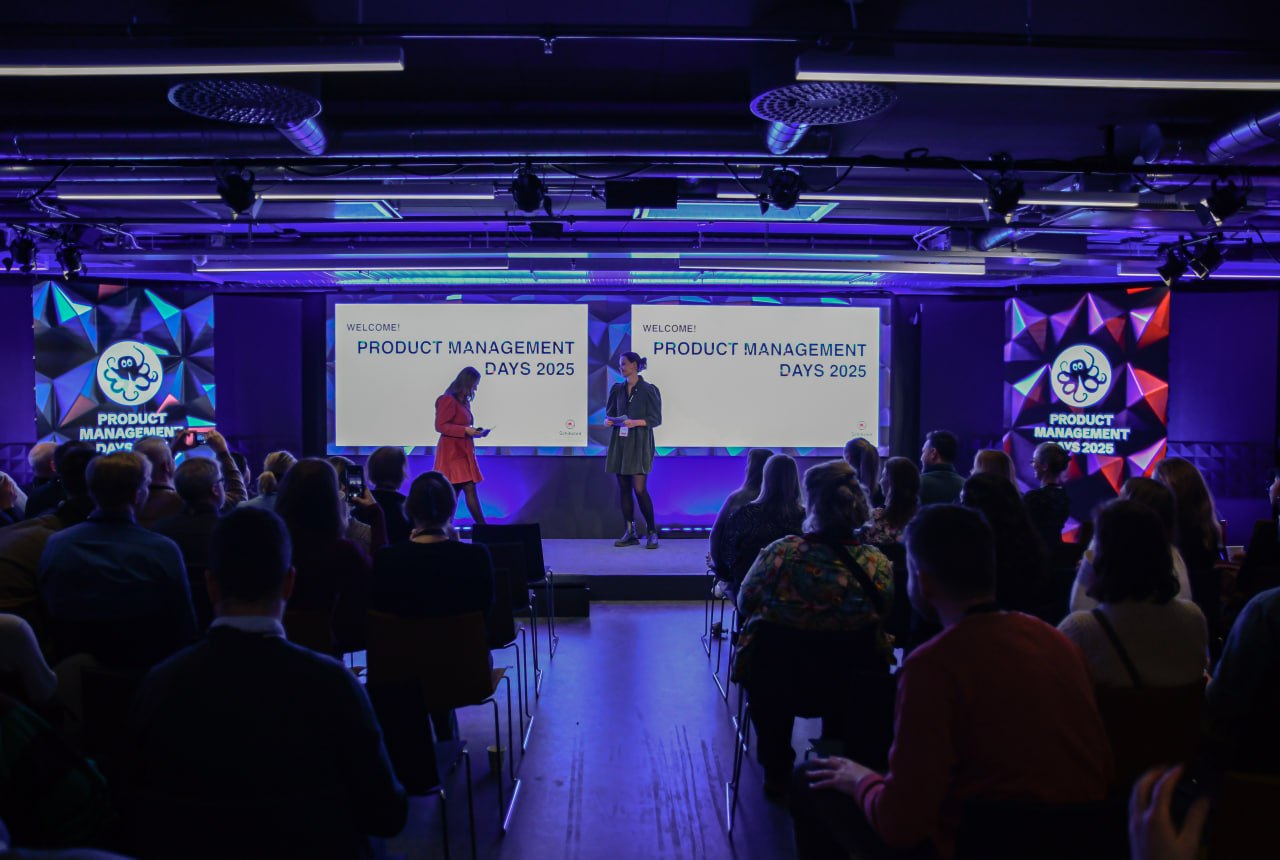A full auditorium facing two screens reading 'Welcome! Product Management Days 2025'.